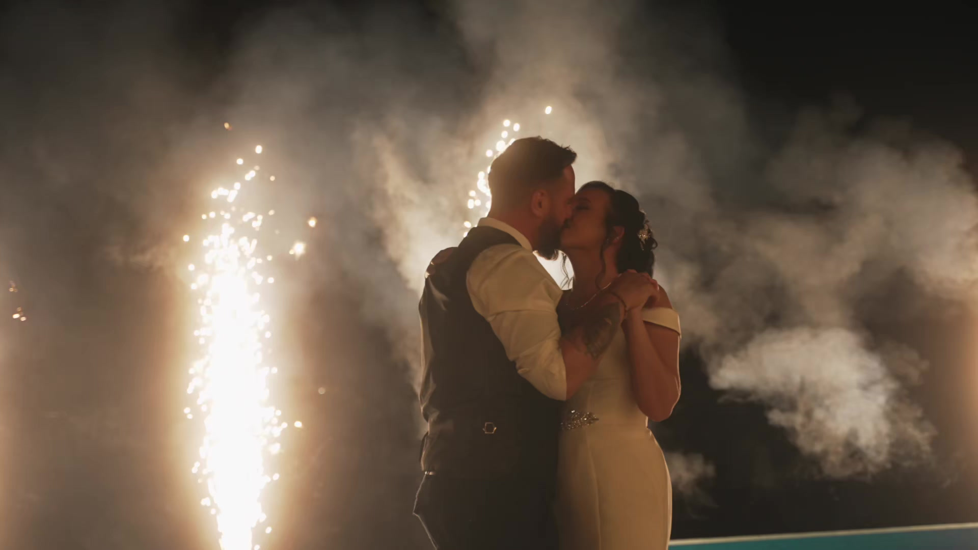A couple kissing during their first dance as fireworks light up the night sky